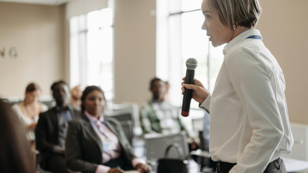 Side view of a businesswoman holding a microphone while addressing an audience at a conference.