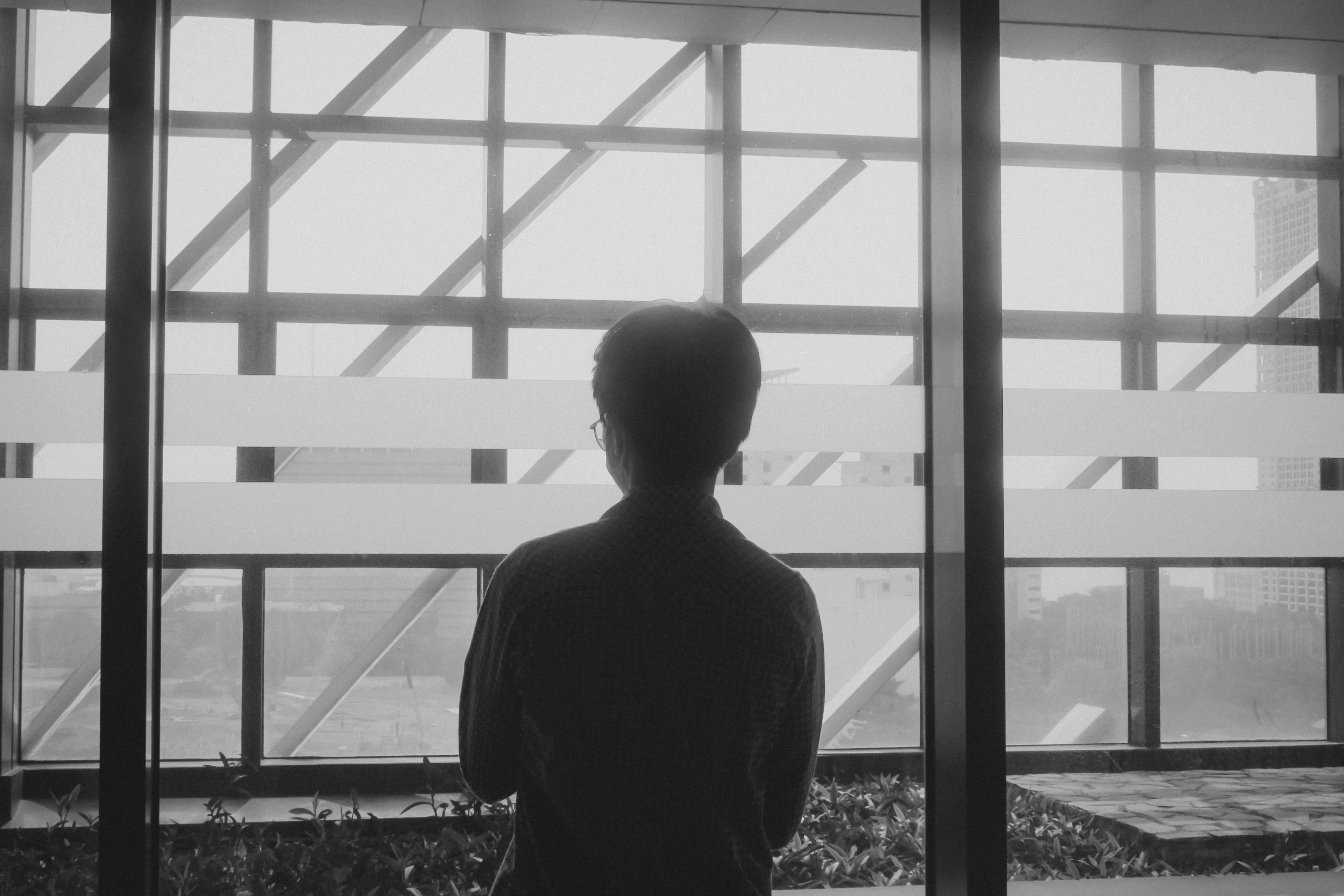 Black and white silhouette of a man gazing out of a modern glass window